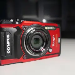 Czerwony, wytrzymały aparat Olympus Tough TG-5 z obiektywem i paskiem na nadgarstek. Gotowy na przygody.