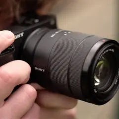 Dłoń trzyma aparat Sony a6400 z obiektywem E 18-135mm, gotowy do testów.