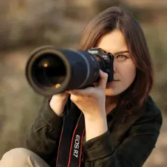 Kobieta z aparatem Canon EOS R7 w rękach, skupiona na kadrze. Jej pasja do fotografii cyfrowej jest widoczna w każdym ruchu.