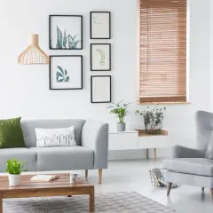 Przytulne **zdjęcia w salonie** z szarą kanapą, fotelem i drewnianym stolikiem. Na ścianie galeria roślinnych grafik.