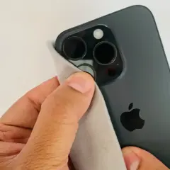 Dłoń czyści obiektywy ciemnego iPhone'a, by aparat w telefonie nie łapał ostrości.
