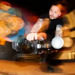 Zdjecie w ruchu: skater z deskorolką Red Bull i operator kamery z lampą błyskową.