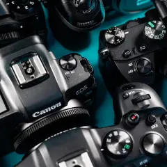 Zbliżenie na kilka aparatów fotograficznych różnych marek, gotowych do testów. Widoczne detale obudowy, pokrętła trybów i logo producentów.