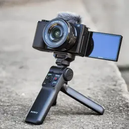 Kompaktowy aparat Sony Alpha ZV-E10 z mikrofonem na gorącej stopce, zamontowany na statywie z uchwytem.