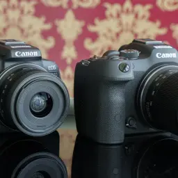 Dwa aparaty Canon EOS R10 i R7 z obiektywami, modele z matrycą canon aps c, stoją na czarnym, błyszczącym blacie.