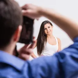Modelka uśmiecha się, pozując do zdjęcia. Fotograf robi jej zdjęcie, pokazując, jak pozowac.