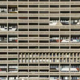 Betonowa fasada bloku mieszkalnego z powtarzalnymi balkonami i oknami. Ta fotografia architektury ukazuje rytm i geometrię modernistycznej budowli.
