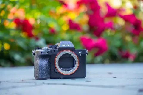 Sony a7 IV premiera. Czarny aparat bez obiektywu na tle rozmytych, kolorowych kwiatów.