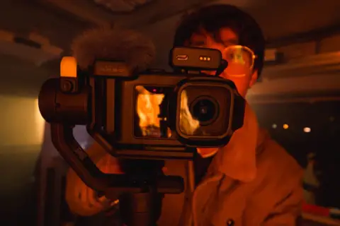 Kamera GoPro z gimbalem, z matrycą 1 cal, nagrywa płomienie. W tle widać osobę w okularach.