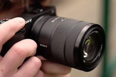 Dłoń trzyma aparat Sony a6400 z obiektywem E 18-135mm, gotowy do testów.
