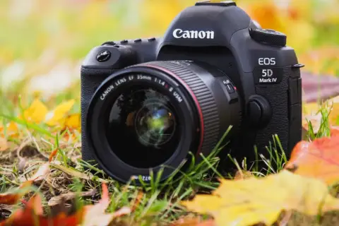 Profesjonalny aparat Canon EOS 5D Mark IV z obiektywem 35mm f/1.4 leży wśród jesiennych liści.