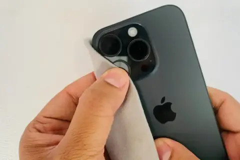 Dłoń czyści obiektywy ciemnego iPhone'a, by aparat w telefonie nie łapał ostrości.