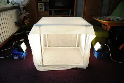 Domowy namiot bezcieniowy DIY, zbudowany z białego materiału i rurek PCV, oświetlony dwoma lampami.
