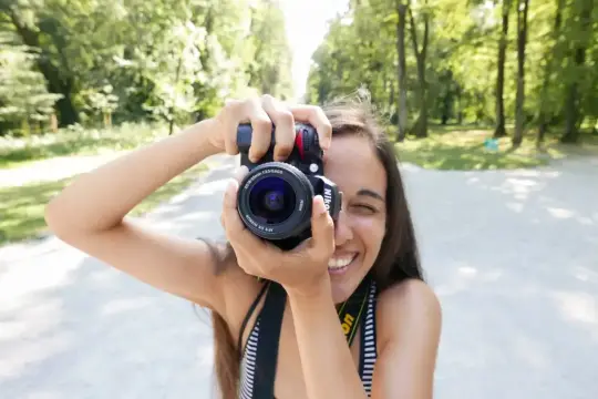 Uśmiechnięta dziewczyna z aparatem i obiektywem kitowym robi zdjęcie w parku.