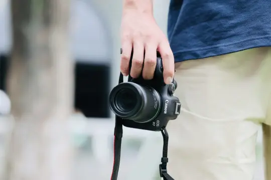 Dłoń trzyma aparat Canon EOS R7 z obiektywem, gotowy do uchwycenia świata dzięki matrycy APS-C.