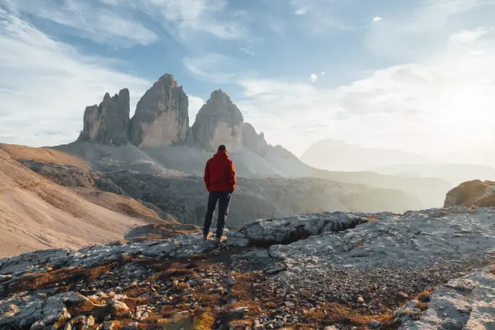 Widok na majestatyczne góry Tre Cime di Lavaredo. Człowiek w czerwonej kurtce podziwia panoramę, ucząc się, jak oddalić zdjęcie, by uchwycić cały krajobraz.