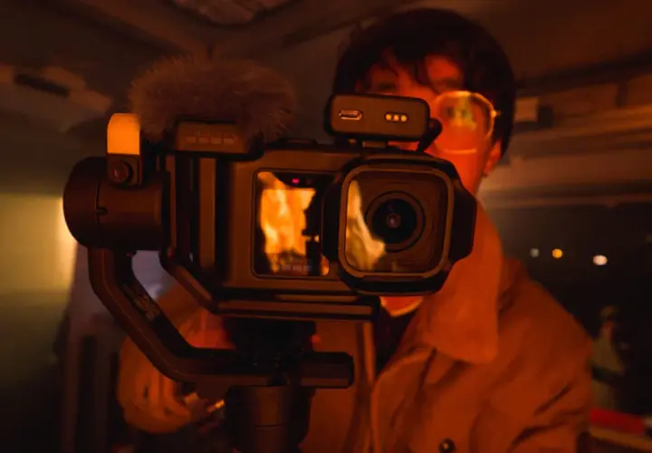 Kamera GoPro z gimbalem, z matrycą 1 cal, nagrywa płomienie. W tle widać osobę w okularach.
