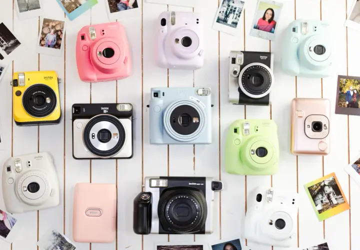Kolekcja kolorowych aparatów do fotografii natychmiastowej Instax, ułożonych na białym tle.