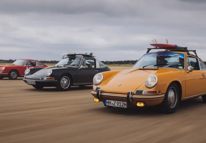 Trzy klasyczne Porsche 911 na plaży, żółte z deskami surfingowymi na dachu. Niesamowita fotografia samochodowa.