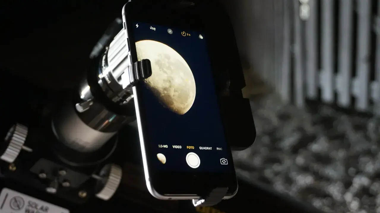 Jak zrobic zdjecie ksiezyca iPhone? Telefon z aparatem zamocowany do teleskopu, na ekranie widoczny Księżyc.