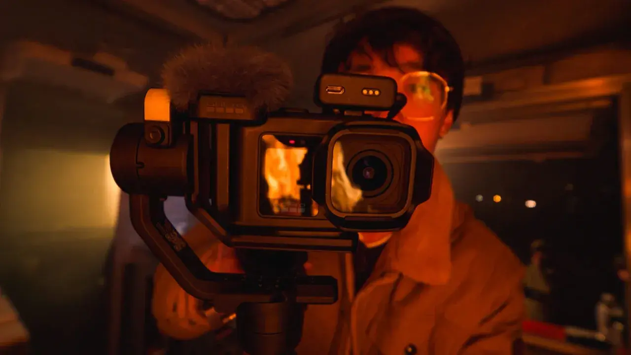 Kamera GoPro z gimbalem, z matrycą 1 cal, nagrywa płomienie. W tle widać osobę w okularach.
