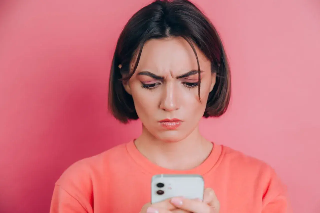 Zmarszczona kobieta patrzy na telefon, zastanawiając się, jak poprawić jakość zdjęć na Instagramie.