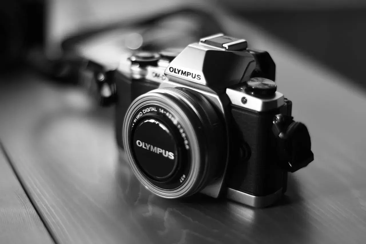 Prześwietlone zdjęcie aparatu Olympus OM-D. Srebrno-czarny korpus i obiektyw z napisem "OLYMPUS".