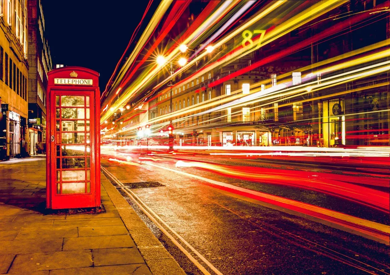 Klasyczna czerwona budka telefoniczna na tle nocnej ulicy z rozmazanymi światłami samochodów, efekt długi czas naswietlania zdjecia.