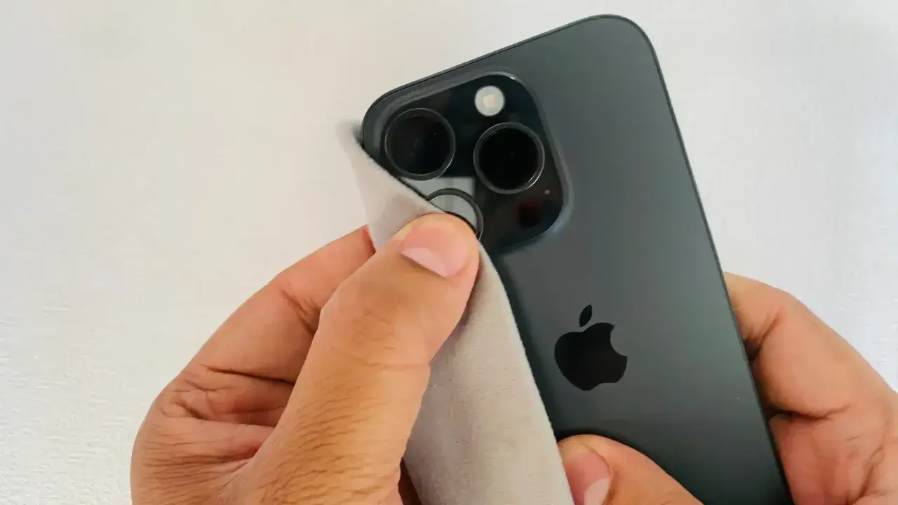 Dłoń czyści obiektywy ciemnego iPhone'a, by aparat w telefonie nie łapał ostrości.