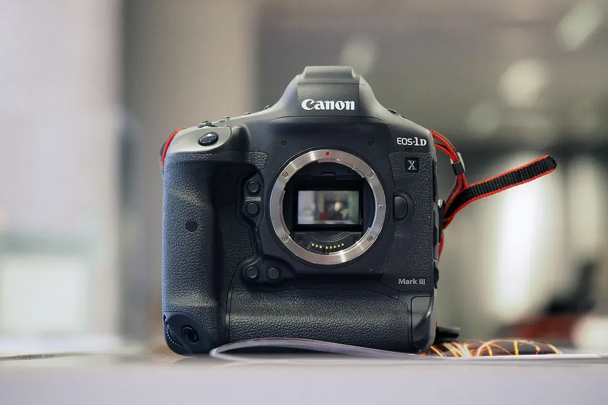 Profesjonalny aparat Canon 1DX Mark III z widocznym mocowaniem obiektywu i paskiem na nadgarstek.