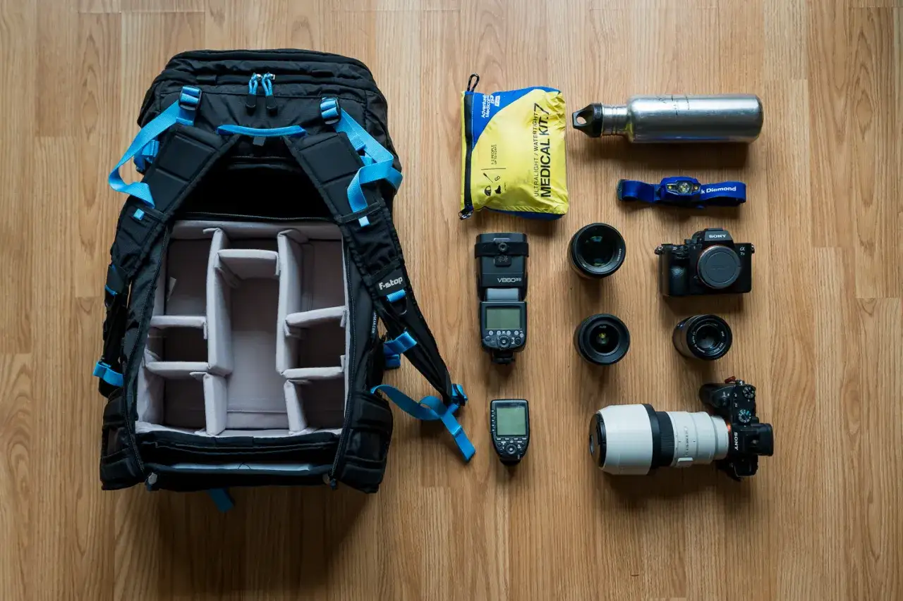Plecak fotograficzny z akcesoriami: aparat Sony, obiektywy, lampa błyskowa, apteczka, butelka. Brak sprzętu Canon vs Nikon.