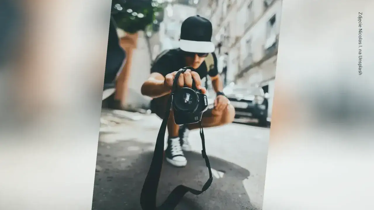Młody fotograf krajobrazu w czapce z daszkiem trzyma aparat przed sobą, gotowy do uchwycenia miejskiego widoku.