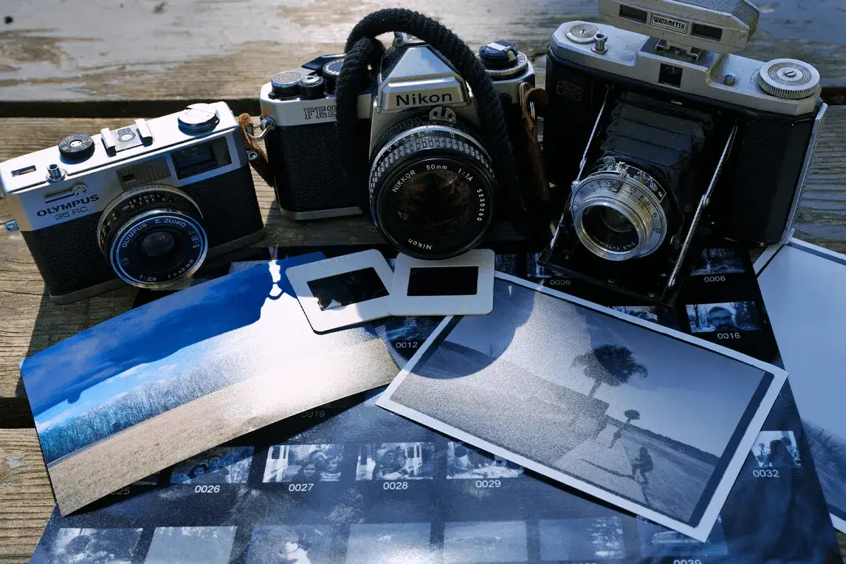 Analogowa fotografia: Olympus, Nikon, Zeiss i odbitki na drewnianym stole. Wspomnienia uchwycone na kliszy.