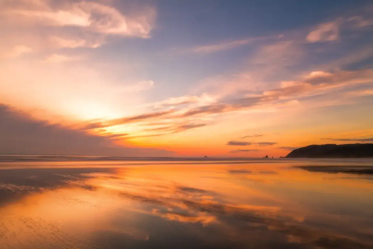 Zachód słońca nad oceanem, idealny do nauki, jak fotografować zachód słońca. Piękne odbicia na mokrym piasku.