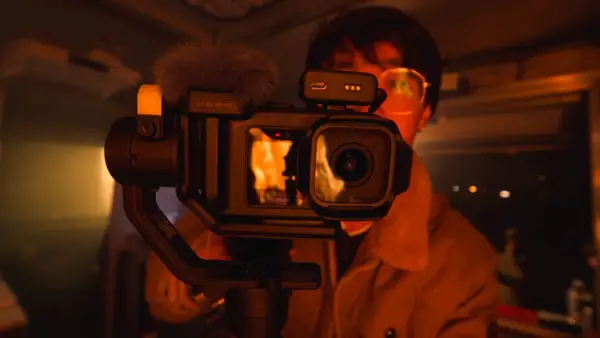 Kamera GoPro z gimbalem, z matrycą 1 cal, nagrywa płomienie. W tle widać osobę w okularach.