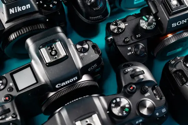 Zbliżenie na kilka aparatów fotograficznych różnych marek, gotowych do testów. Widoczne detale obudowy, pokrętła trybów i logo producentów.